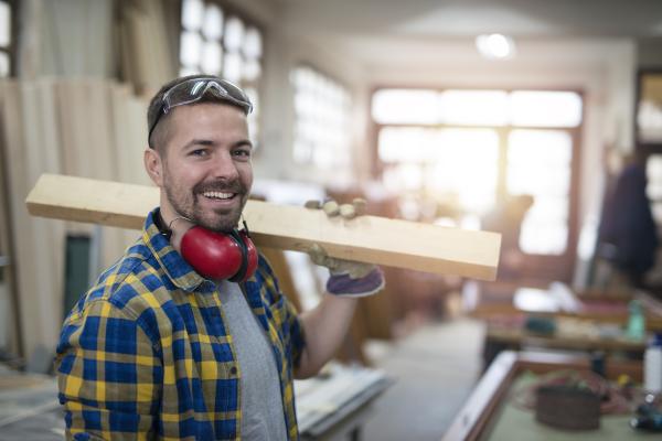 Charpentier portant un casque anti-bruit et une planche de bois sur l'épaule